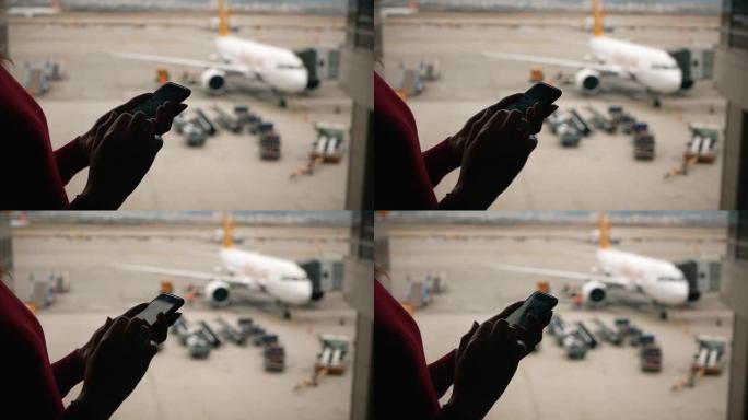 女子双手用智能手机在机场航站楼窗外的客机背景上