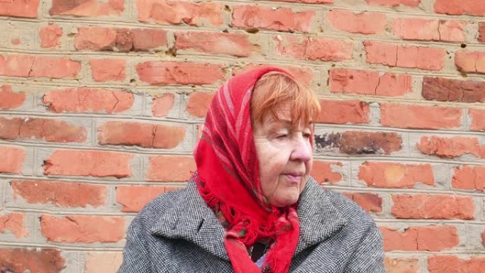 穿着红围巾的老妇在砖墙背景上。母亲节。祖母。人。年龄。面部表情。