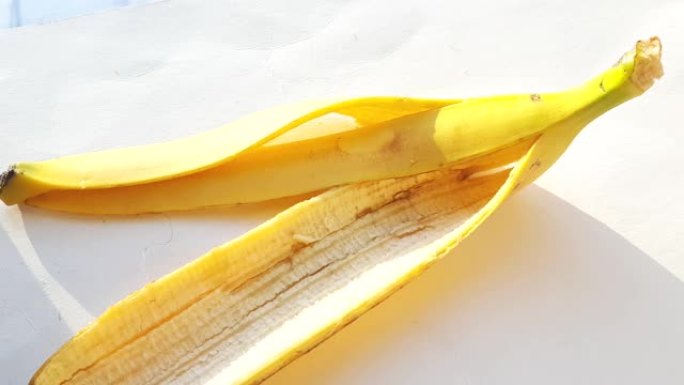香蕉皮在明亮的阳光下的白色背景上，女人的手将果皮放在桌子上