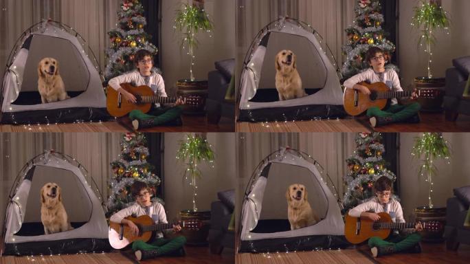 一个小男孩和他的狗宠物的肖像，弹吉他，一起庆祝圣诞节。