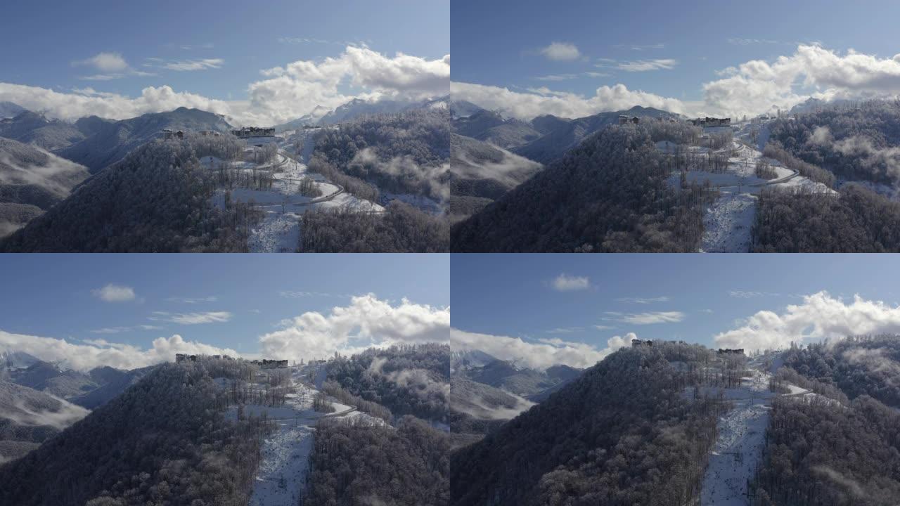 从着陆飞行无人机，在多云的天空景观上，雪峰上的山村。鸟瞰雪山度假村的蜿蜒道路。福吉天空上令人叹为观止
