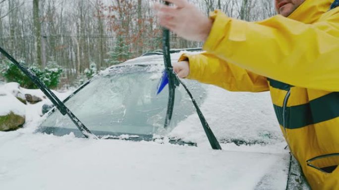 成熟的人从冰雪中清洁挡风玻璃刮水器叶片。