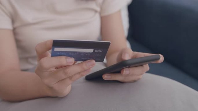 年轻的亚洲妇女使用数字移动设备手持信用卡并在线购买