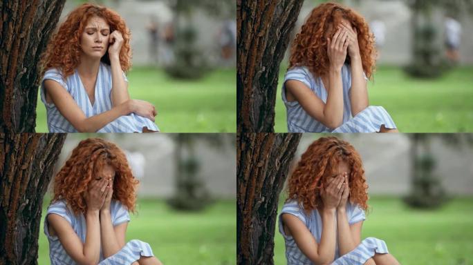 沮丧的红发女孩在公园哭泣和遮住脸