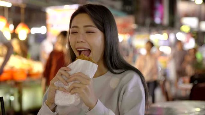 亚洲妇女在夜市享受鸡柳和街头美食