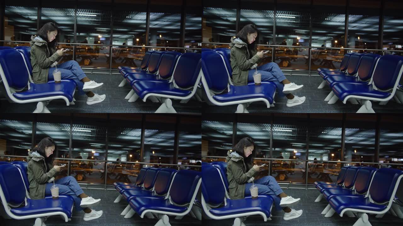 4k视频片段，一名年轻女子在夜间在出发航站楼机场触摸并使用智能手机等待航班。