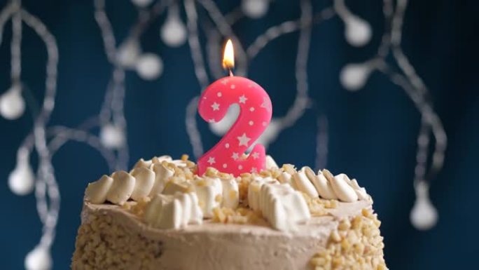 蓝色背景上有2个数字粉色蜡烛的生日蛋糕。蜡烛吹灭了。慢动作和特写视图
