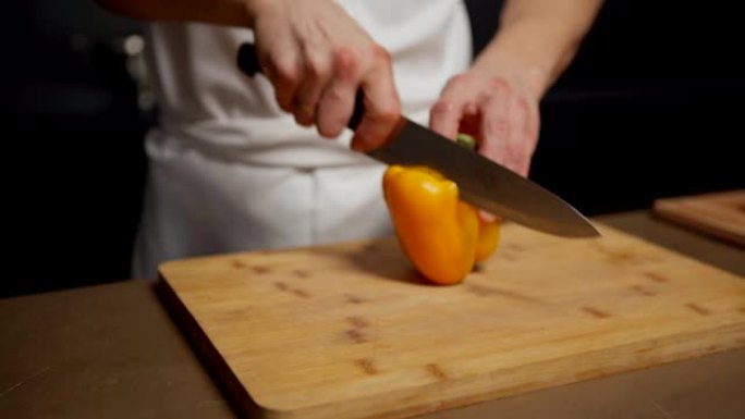 从上方跟踪拍摄厨房桌子上新鲜食材的特写镜头，厨师的手拿着黄色的甜椒，用刀切开