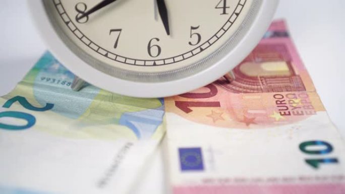 白色闹钟，白色桌子上有黑色箭头和欧元钞票