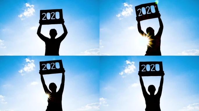 女人的剪影拿着回收纸板，2020文字在蓝天背景和阳光透过文字。新年和庆祝活动的概念。
