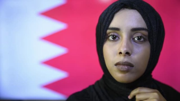特写年轻美丽的穆斯林女孩戴着头巾，站在卡塔尔国旗上