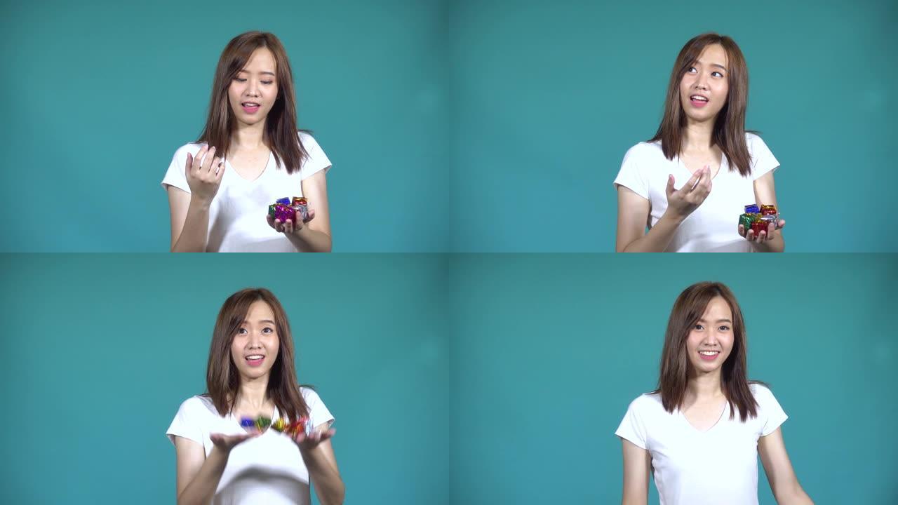 亚洲快乐美丽可爱的年轻女子青少年她手边扔小礼品盒，看着工作室里的相机，孤立在蓝色背景上，4k视频解决