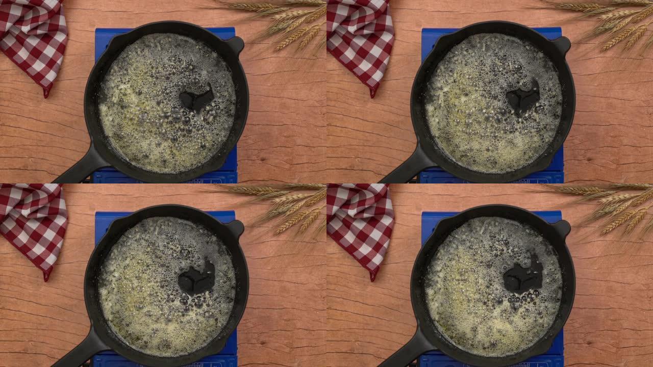 煤气炉上铁锅的俯视图拍摄，烤架表面融化了大块黄油。