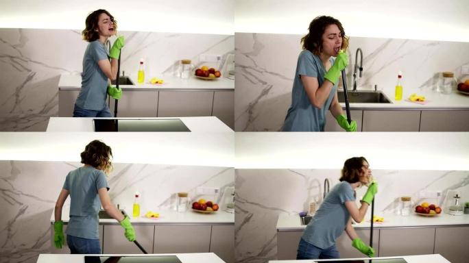 快乐的年轻女人可爱的家庭主妇正在厨房里用拖把洗地板，跳舞唱歌，享受家务。人、现代生活方式与青年观念