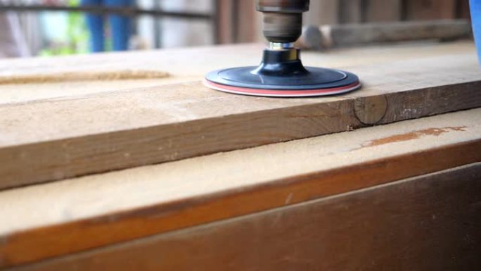 木材加工的特写。面目全非的木匠在他的车间里工作。工匠加工一些木制产品的工件。背景模糊，木屑飞来飞去。