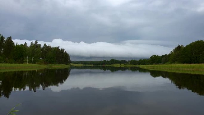 平静的夏夜日落美景。湖岸绿树和植物反射在水晶干净的镜面水面。天空覆盖着厚重的雷云。慢动作。