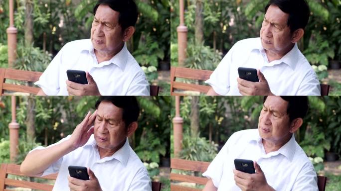 老人坐在公园长椅上使用手机。亚洲男人，非常混乱的情绪。
