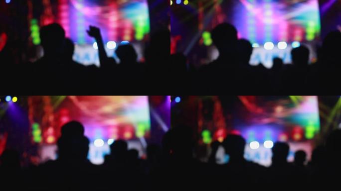 慢动作，人们在大厅舞台前的摇滚音乐会上聚会，欢呼和示手的剪影。彩色蓝色舞台灯光，带发光二极管灯的舞台