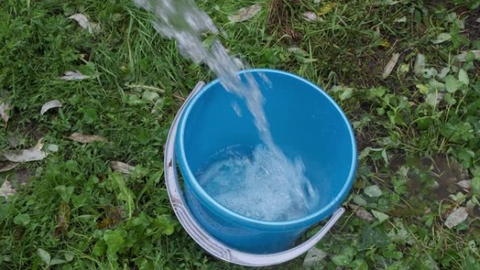 在夏天的花园中，该男子将水倒入塑料蓝色的水桶中。