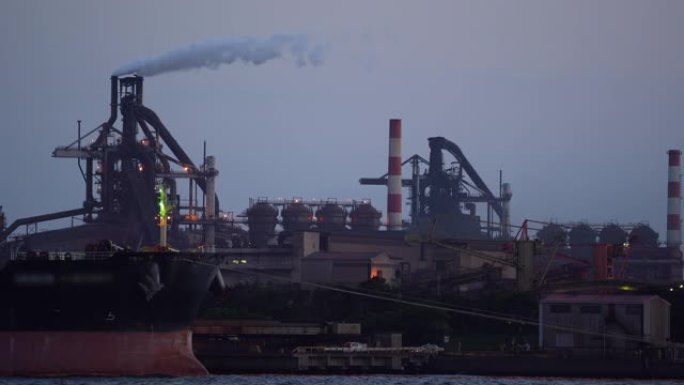 工业船在煤电厂前的码头卸煤，而烟雾在黄昏时从烟囱排出