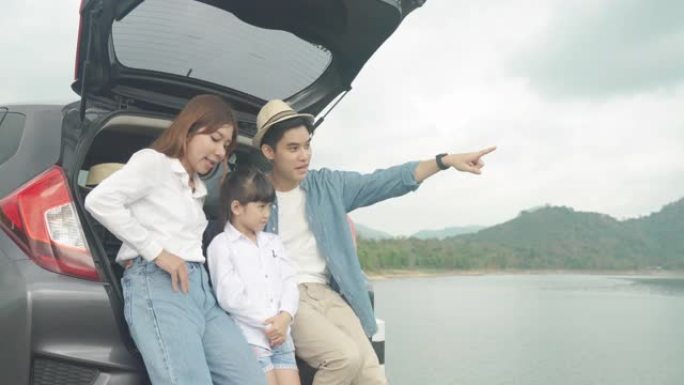 亚洲家庭与父亲，母亲和女儿坐在汽车上的肖像，并通过smrtphone在度假时一起欣赏湖景和山景。幸福