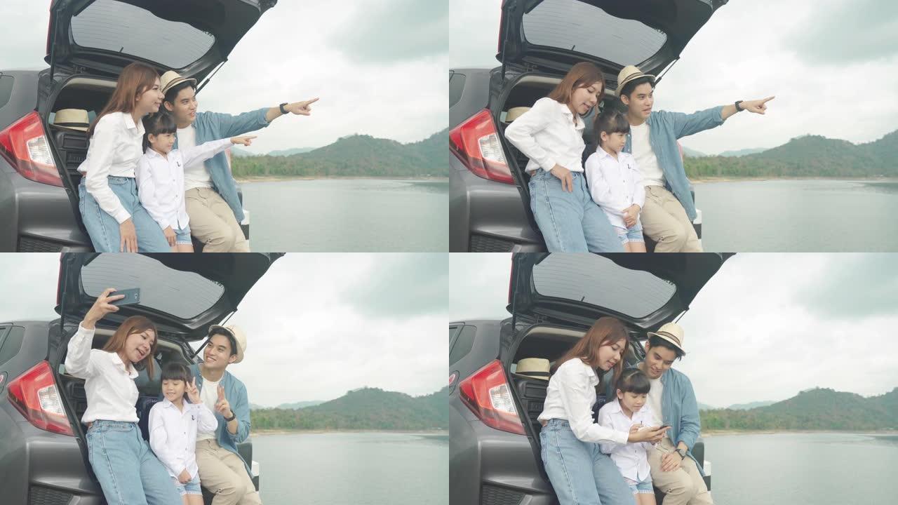 亚洲家庭与父亲，母亲和女儿坐在汽车上的肖像，并通过smrtphone在度假时一起欣赏湖景和山景。幸福