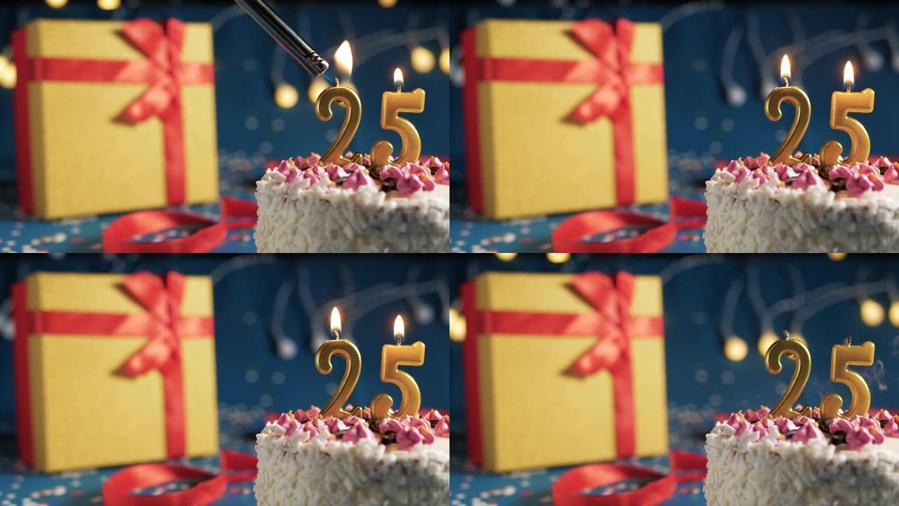 白色生日蛋糕25号点火器燃烧的金色蜡烛，蓝色背景带灯和用红丝带绑起来的礼物黄色盒子。特写