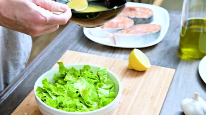 将女性手在家庭厨房中的特写镜头添加到素食叶沙拉酱中，并在木制切菜板上与勺子混合