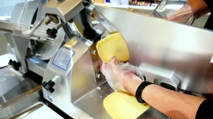 女人使用专业的电动食品切片机，配有一次性手套，切片奶酪