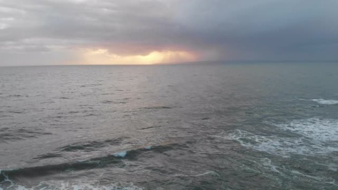 风雨如磐的灰色天空下波涛汹涌的海浪的空中后退镜头，太阳在云层后面发光