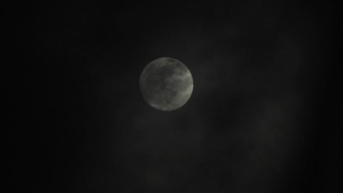 阴暗的夜晚满月。云彩从月亮掠过，实时拍摄。