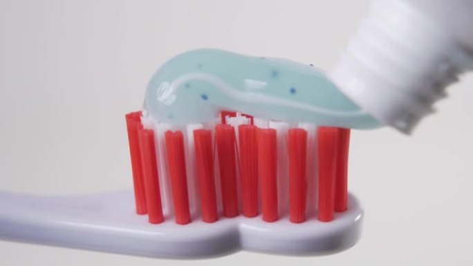 蓝色牙膏的特写覆盖了塑料牙刷的红色刷毛