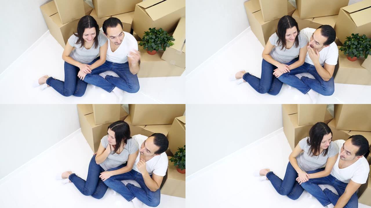 幸福的夫妻夫妇坐在新公寓靠近一堆纸板的地板上的俯视图。