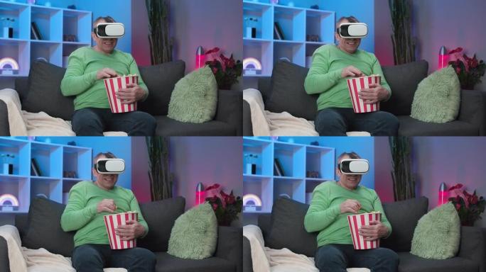 高个子白人男子使用虚拟现实耳机观看视频，坐在沙发上吃爆米花在房间里