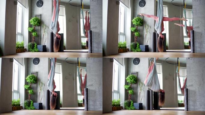 熟练的年轻女子倒吊在吊床上，在反重力瑜伽工作室做伸展运动