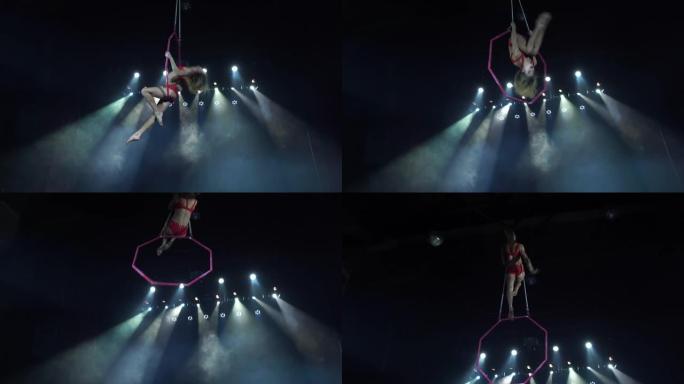 舞台上苗条性感的女性空中杂技演员，背景上有聚光灯的空中箍