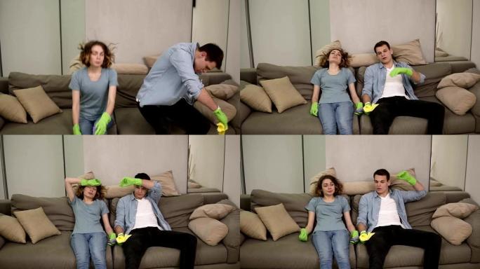 筋疲力尽的白人年轻夫妇在清洁后倒在沙发上，清洁后感到疲倦，额头上挥出汗水。呼气。戴着绿色橡胶手套。慢