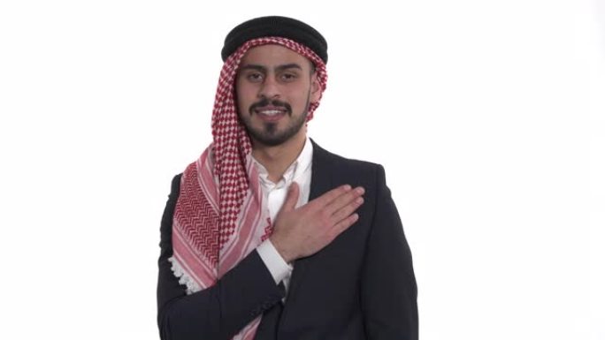 积极的阿拉伯年轻人的肖像看着相机，微笑着触摸他的胸部。孤立，在白色背景上