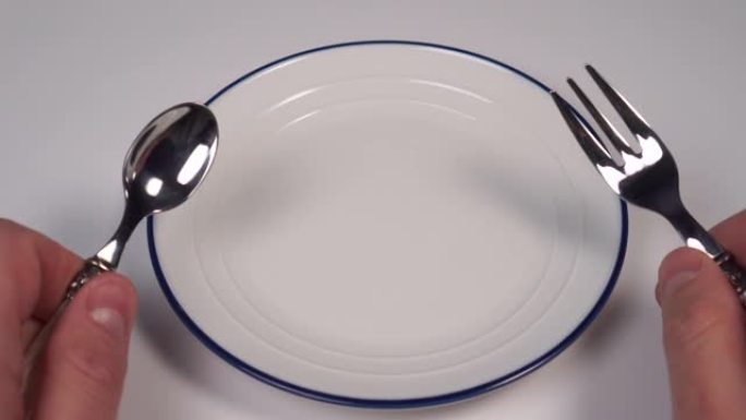 餐厅桌子上有蓝色边框的白色盘子。在甜点叉子和勺子的手中
