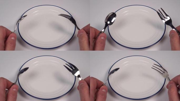 餐厅桌子上有蓝色边框的白色盘子。在甜点叉子和勺子的手中