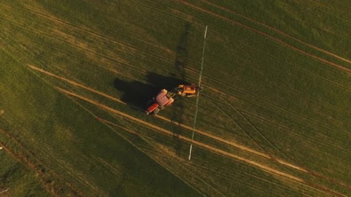 日落时用喷雾器，除草剂和农药在田间喷洒的农用拖拉机的鸟瞰图。农用机械向绿地喷洒杀虫剂，农业自然季节春