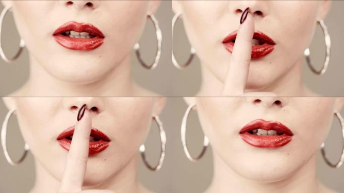 秘密。关闭红色唇膏和红色指甲。手指指着嘴。