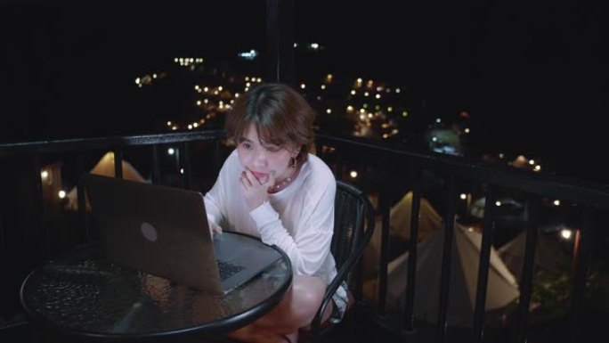 迷人的亚洲女性工作到很晚，在黑暗中工作场所的电脑显示器桌面前的桌子上认真地喝咖啡