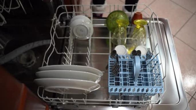 家庭主妇把脏盘子放在洗衣机的篮子里，然后关上。女人用脏餐具灌装洗衣机，家庭主妇的日常厨房工作