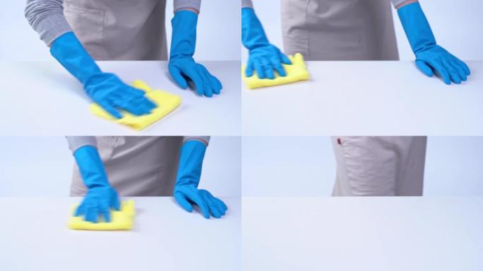 年轻的女管家正在用蓝色手套，喷雾清洁剂，湿的黄色抹布在围裙上清洁白色桌子。