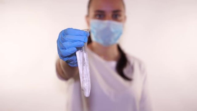 医生戴着蓝色手套的手拿着一个用过的避孕套，白色背景上有精子。精子乳胶和防止怀孕