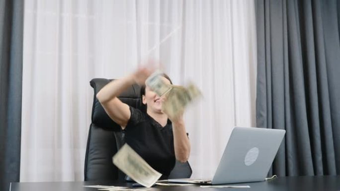 快乐的富婆撒美元钞票堆。成功的女老板在办公室里零钱。女性坐在办公桌前向空中扔钱