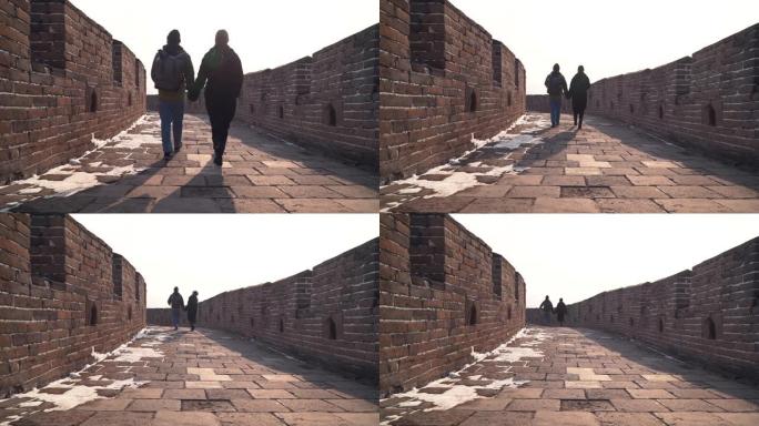 夫妻一起探索中国的长城，在宽阔的通道的石头路面上低摄像头。游客牵手下来，冬天享受空旷的慕田峪遗址