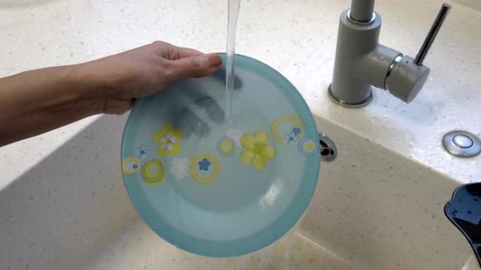 一个女人的特写镜头，在厨房水槽的水流下洗了一个漂亮的蓝色盘子，上面画了黄色的花。不露面。概念。4K