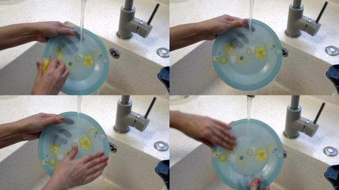 一个女人的特写镜头，在厨房水槽的水流下洗了一个漂亮的蓝色盘子，上面画了黄色的花。不露面。概念。4K